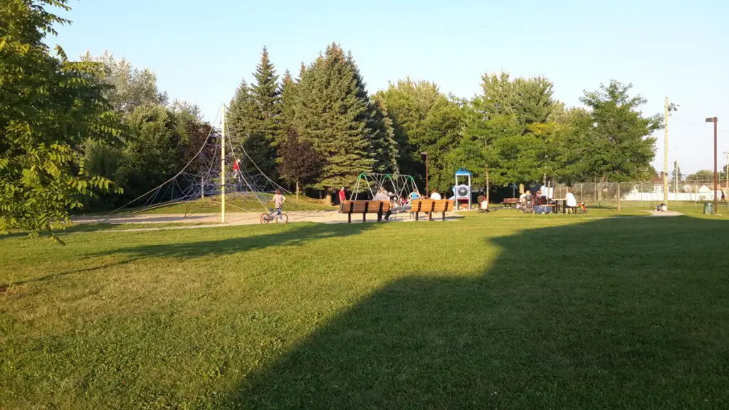 Parc verdoyant avec aire de jeux, balançoires et bancs, au cœur d’un quartier de maisons de ville à Laval.