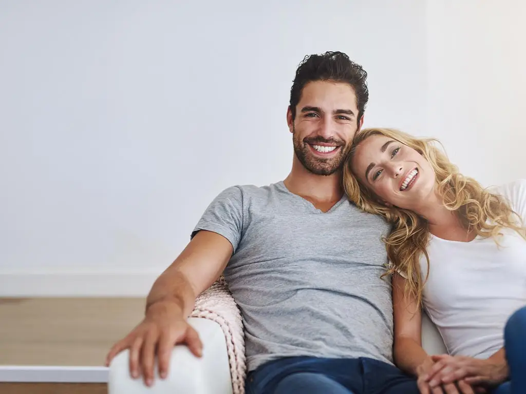 Couple souriant assis sur un canapé dans un intérieur lumineux et épuré, illustrant un projet de maisons de ville neuves