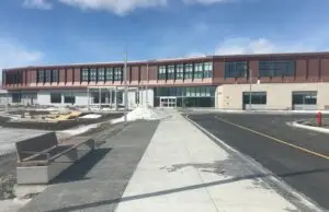 Bâtiment moderne à deux étages, façade vitrée, entrée centrale, stationnement et trottoir en construction.