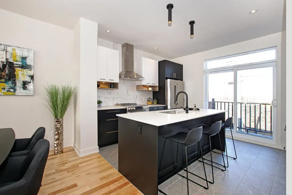 Cuisine moderne avec îlot, armoires noir et blanc et grande fenêtre dans une maison de ville à Laval