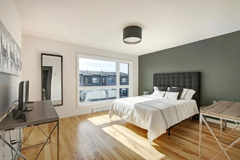 Chambre lumineuse avec grande fenêtre, mobilier moderne et plancher de bois, maison de ville à Laval