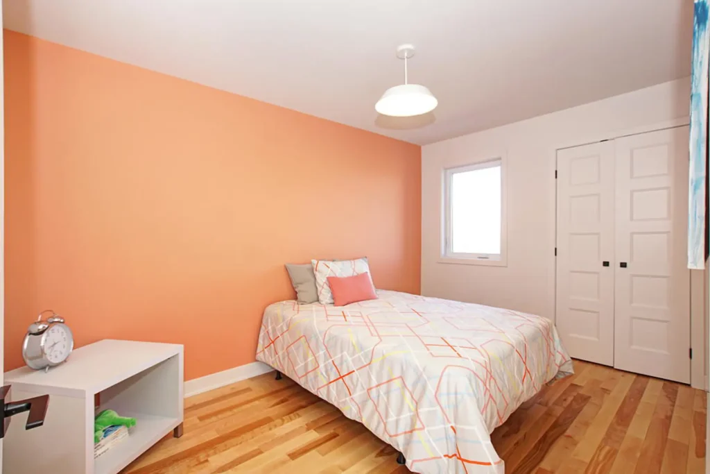 Chambre lumineuse avec mur orange, lit double, plancher en bois et déco épurée, maison de ville à Laval
