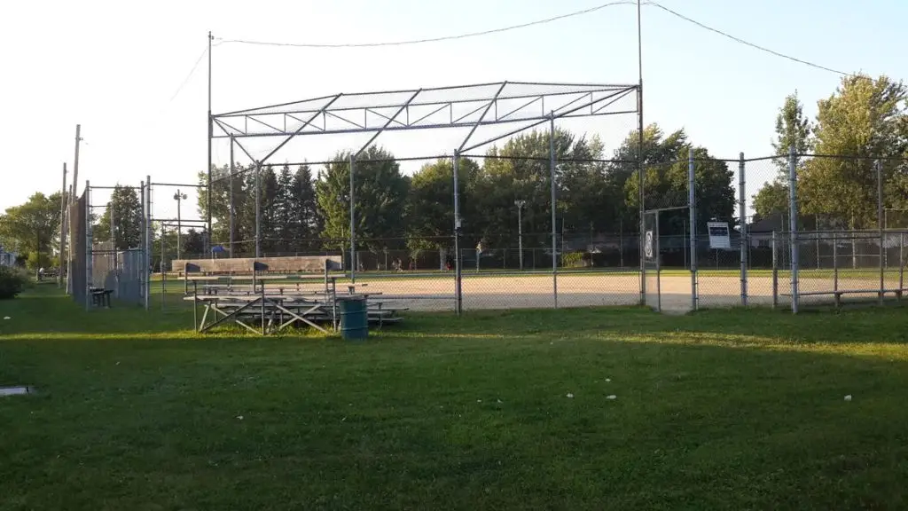 Terrain de baseball clôturé avec estrades, entouré d’arbres dans un parc résidentiel ensoleillé
