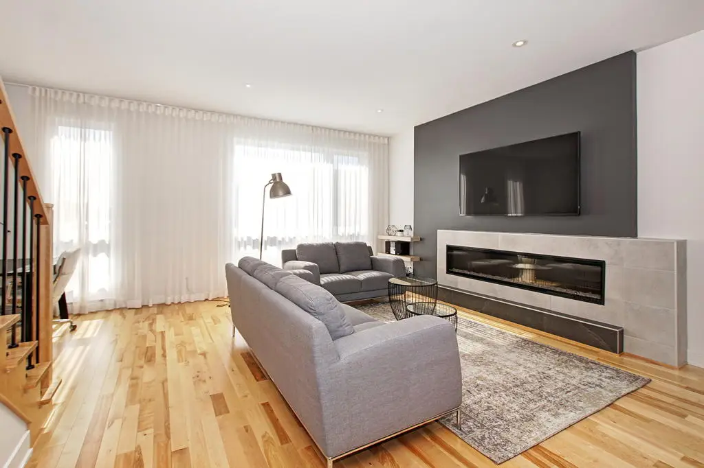 Salon lumineux avec canapé gris, foyer moderne et grandes fenêtres dans une maison de ville à Laval