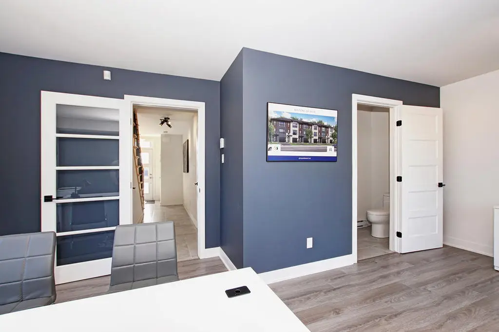 Pièce moderne aux murs bleus avec mobilier et affiche d’un projet de maisons de ville neuves à vendre à Laval