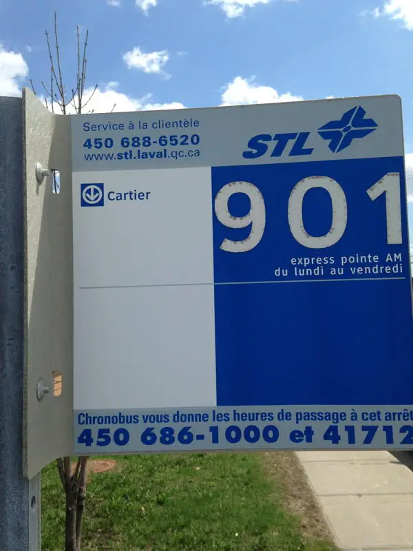 Panneau d’arrêt d’autobus STL à Laval indiquant la ligne 901 express pointe, sous ciel bleu avec arbre et trottoir.