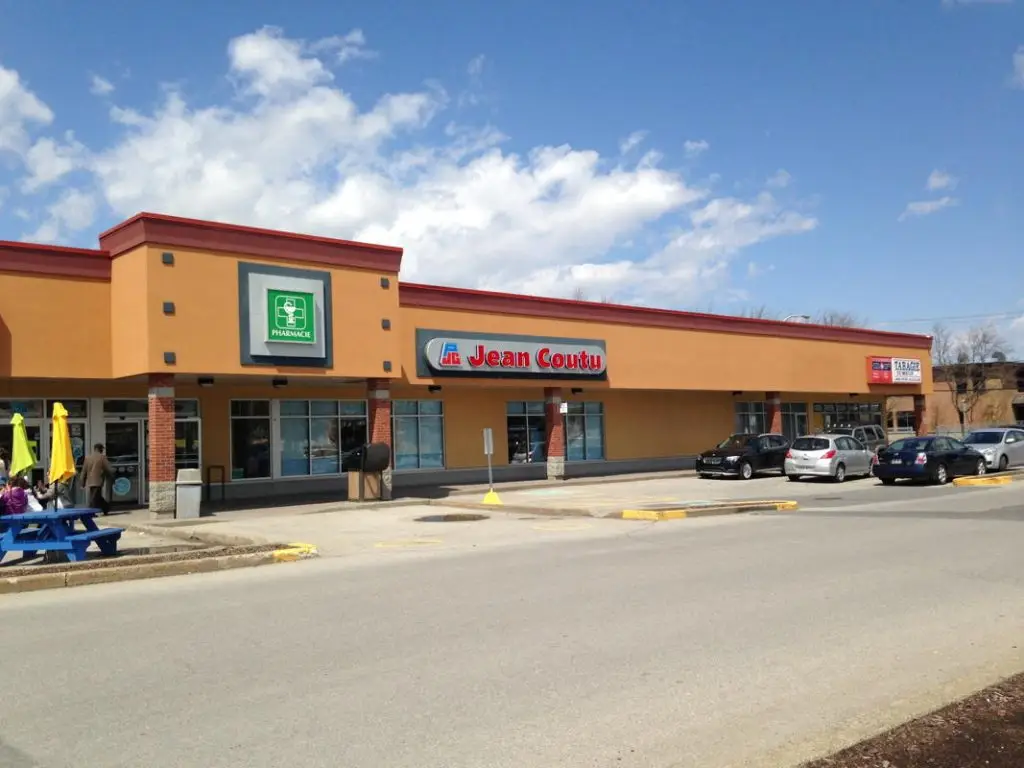 Façade d’une pharmacie Jean Coutu dans un centre commercial avec stationnement et ciel dégagé