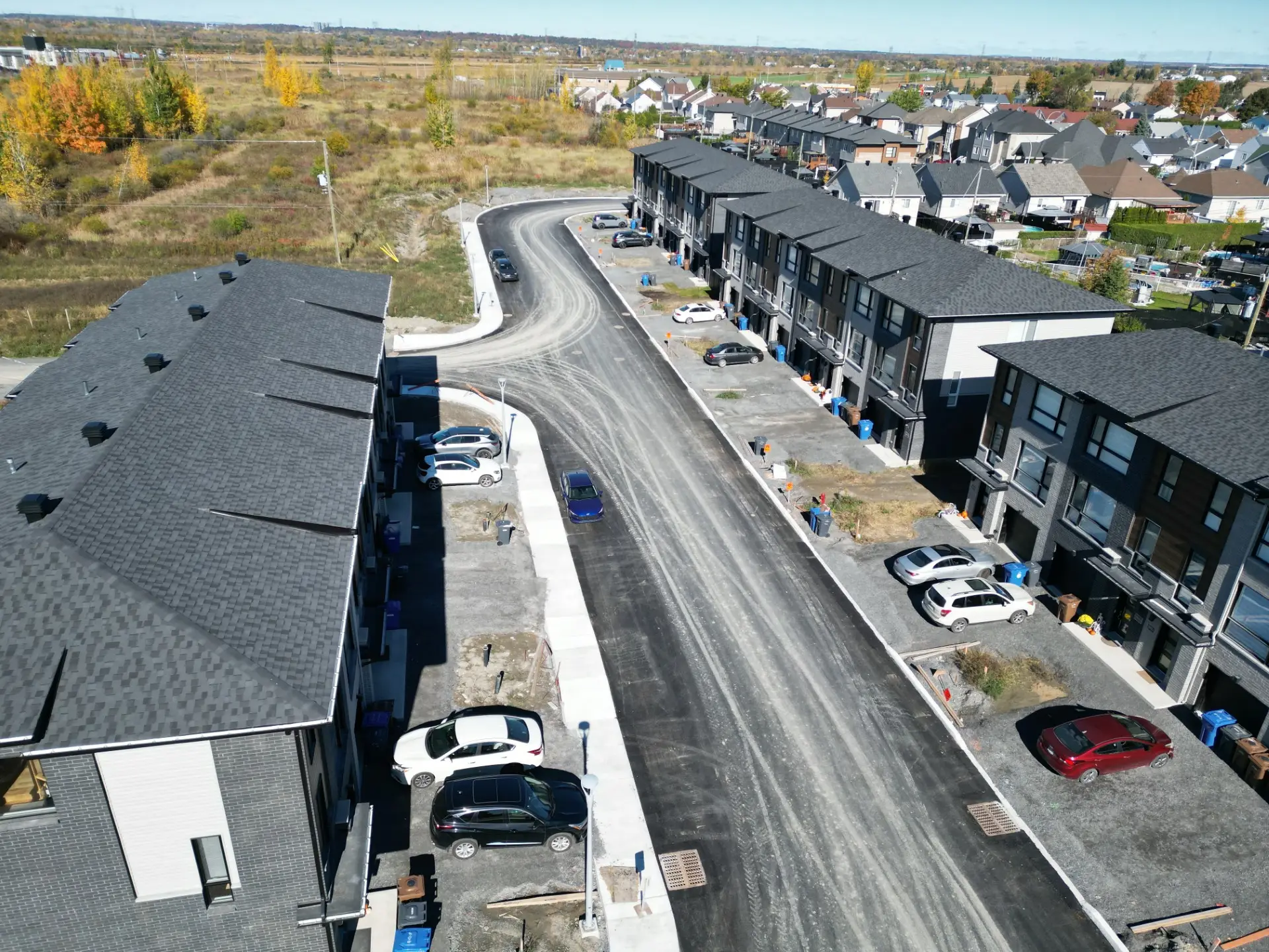Vue aérienne d’un projet de maisons de ville neuves à Laval le long d’une rue en construction avec stationnements et façades modernes
